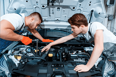 Two mechanics working under the hood of a vehicle